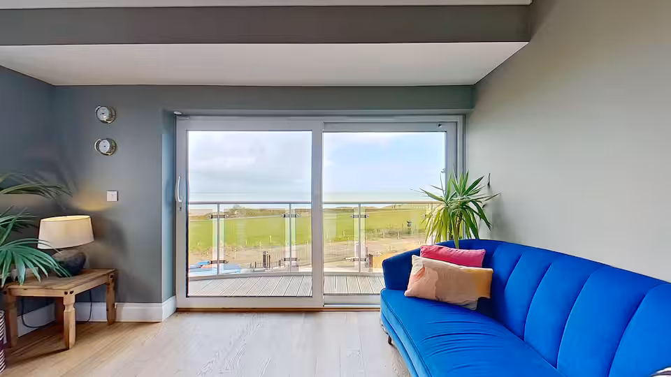 Living room with blue velvet sofa opening onto sea-facing balcony