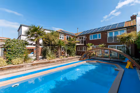 Exterior view of beach house with heated pool, palm trees and solar panels